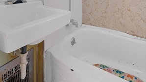 Ein Badezimmer mit einem weißen Waschbecken, einer Badewanne und einer Blumendusche liegen am Waschbecken. Ein Spiegel befindet sich  über dem Waschbecken.