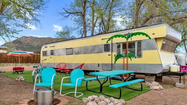 Ein klassischer Wohnwagen mit Picknicktischen und -stühlen, einem Grill und einem kleinen Garten.