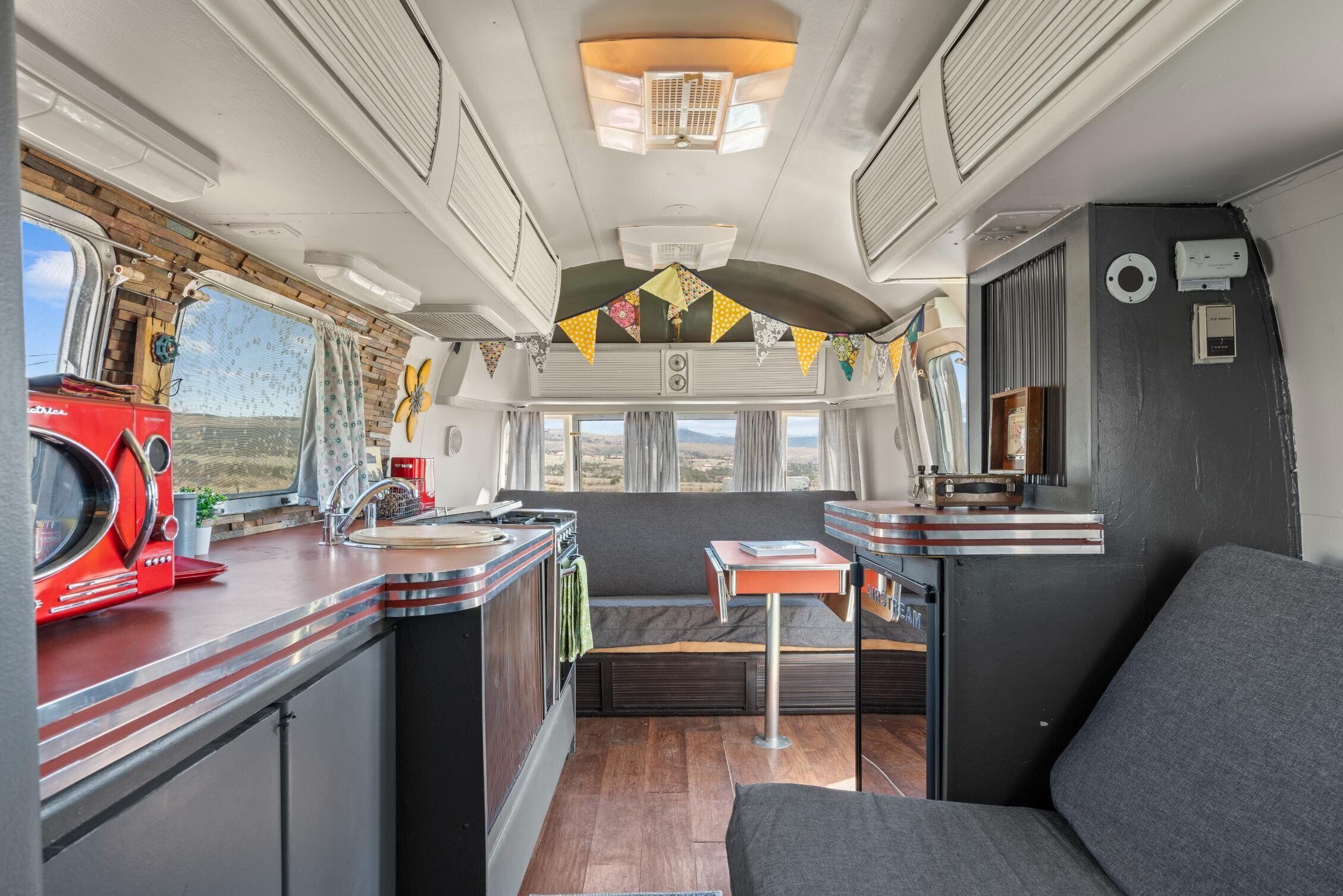 Interior compacto de una autocaravana con kitchenette, zona de estar y ventana con vistas al exterior.