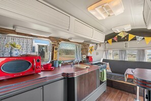 A compact RV kitchen with a red microwave, a sink, and a stove. - Vintage Trailer Stay | Unique Red Miracle | Cañon City (Canon City)