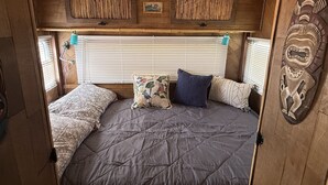 A cozy interior with a bed, pillows, and a decorative wall piece. - Vintage Tiki Motorhome | Unique Stay in Cañon City, CO (Canon City)