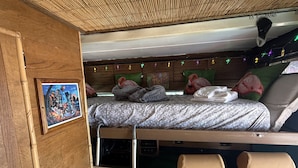 A compact RV interior with a bed, a ladder, and a small seating area. - Vintage Tiki Motorhome | Unique Stay in Cañon City, CO (Canon City)