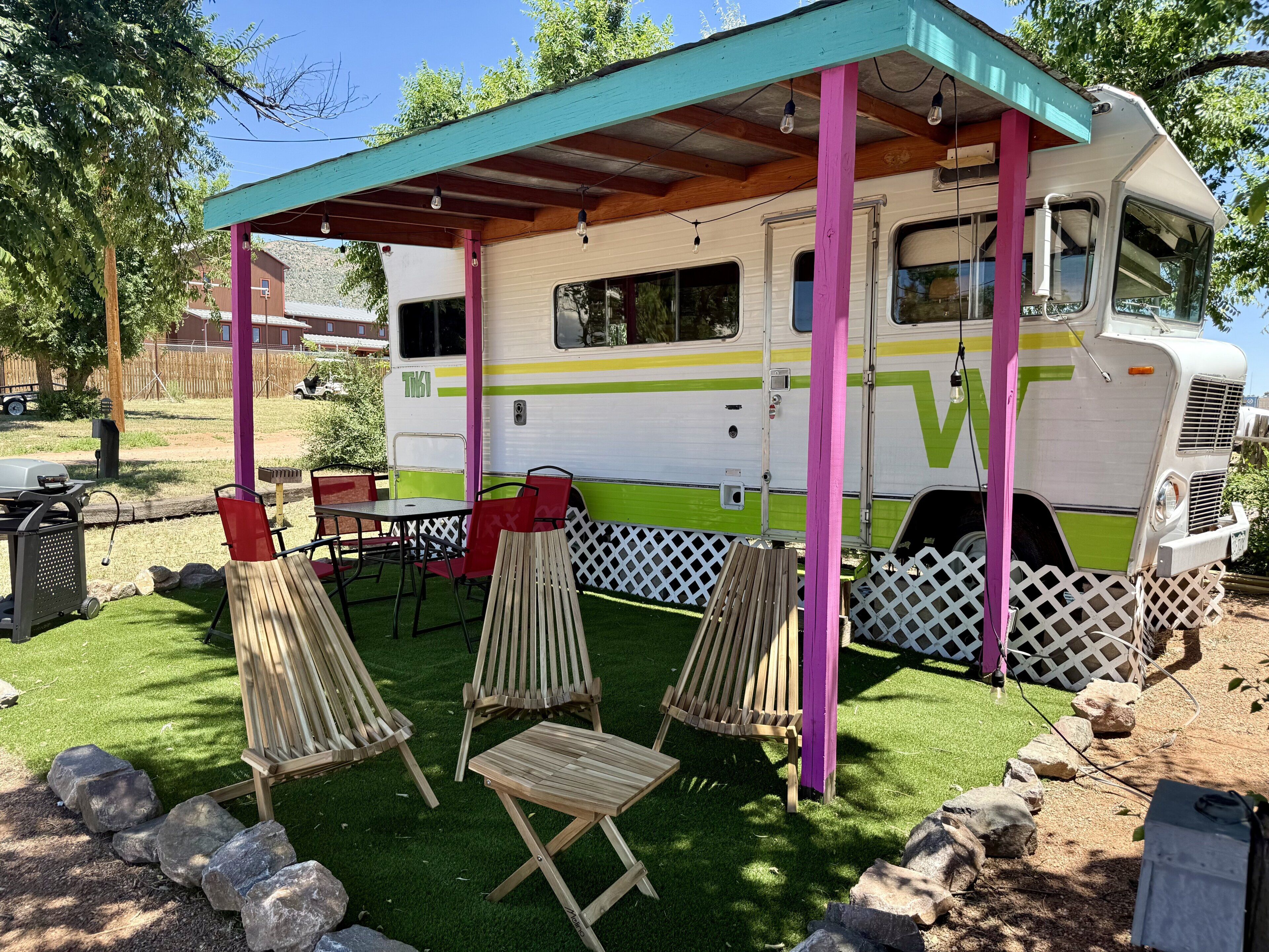 Un vehículo recreativo con un porche cubierto, mobiliario exterior y una parrilla.