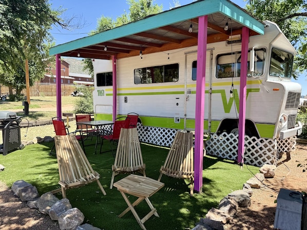 Un vehículo recreativo con un porche cubierto, mobiliario exterior y una parrilla.