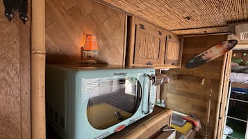 A compact kitchen with a vintage microwave, wooden cabinets, and a bamboo ceiling.