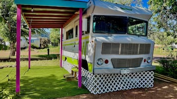 A vintage camper van parked under a covered area with a white lattice base.
