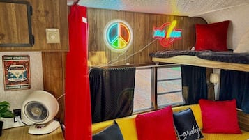 A room with a bunk bed, a fan, a peace sign, and a neon sign.