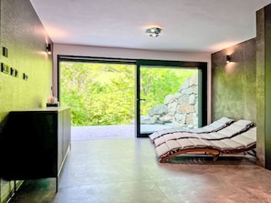 A modern bedroom with a bed, a desk, and a view of greenery through a large window. - Pod hvězdami by Interhome (Strážné)