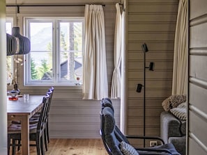 A room with a dining table, chairs, a lamp, a window with curtains, a sofa, and a floor lamp.