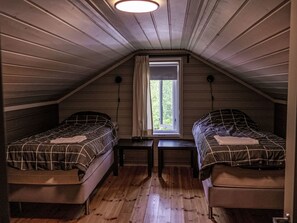A small attic bedroom with two beds, a window, and a wooden floor.