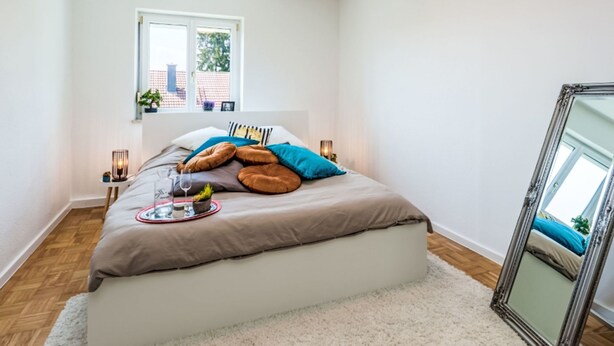 A bedroom with a bed, a window, a mirror, and a small table with a lamp. - 1OG "R" Helle 80m² 3-Zimmer Wohnung näh by Interhome (Freilassing)