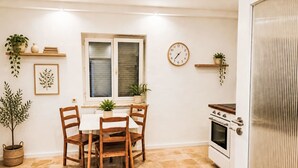 A dining area with a table and chairs, a window with blinds, a clock, and a kitchen with an oven. - 1OG "R" Helle 80m² 3-Zimmer Wohnung näh by Interhome (Freilassing)