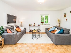 A living room with two grey sofas, a coffee table, a TV, and a window with a view of trees. - 1OG "R" Helle 80m² 3-Zimmer Wohnung näh by Interhome (Freilassing)