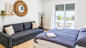 A bedroom with a grey sofa, a bed with a purple bedspread, a large mirror with a golden frame, and a view of the outdoors through a sliding door. - 1OG "R" Helle 80m² 3-Zimmer Wohnung näh by Interhome (Freilassing)