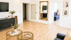 A modern living room with a wooden floor, a dark sofa, a round coffee table, and a TV mounted on the wall. - 1OG "R" Helle 80m² 3-Zimmer Wohnung näh by Interhome (Freilassing)