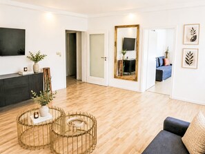 Ein modernes Wohnzimmer mit Holzboden, einem dunklen Sofa, einem runden Couchtisch und einem an der Wand befestigten Fernseher.