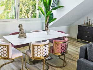 En matplats med ett vitt bord, fyra stolar med guld- och rosa klädsel, en Buddha-staty och en växt.