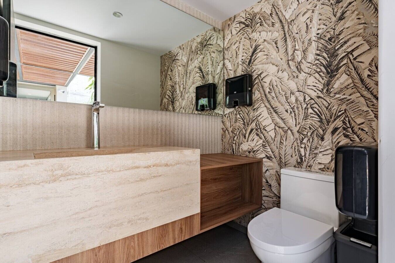 Un baño con tocador de madera, inodoro y pared con diseño de hojas.