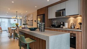 Een moderne keuken met een centraal eiland, barkrukken, een magnetron, een koelkast en een gasfornuis.