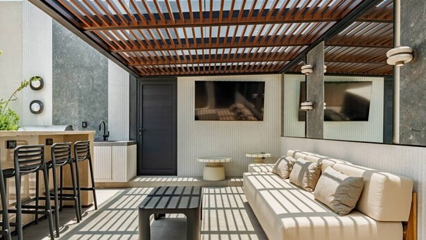 Een moderne buitenruimte met een bank, stoelen, een tafel en een keukenhoek.