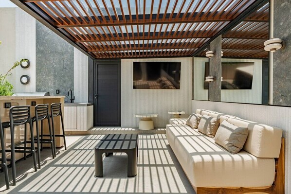 A modern outdoor living space with a sofa, chairs, a table, and a kitchen area. - Condesa Penthouse with Rooftop Terrace & BBQ (Mexico City)