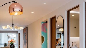 Een moderne woonkamer met een bank, een glazen salontafel en een eethoek op de achtergrond.