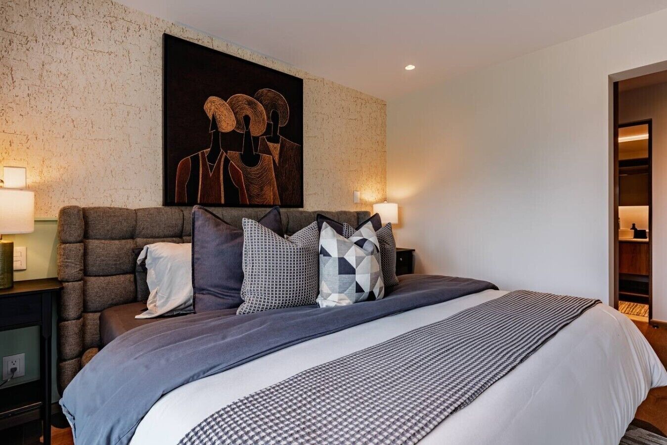 Un dormitorio moderno con una cama grande, una pared con textura y un cuadro sobre la cama.