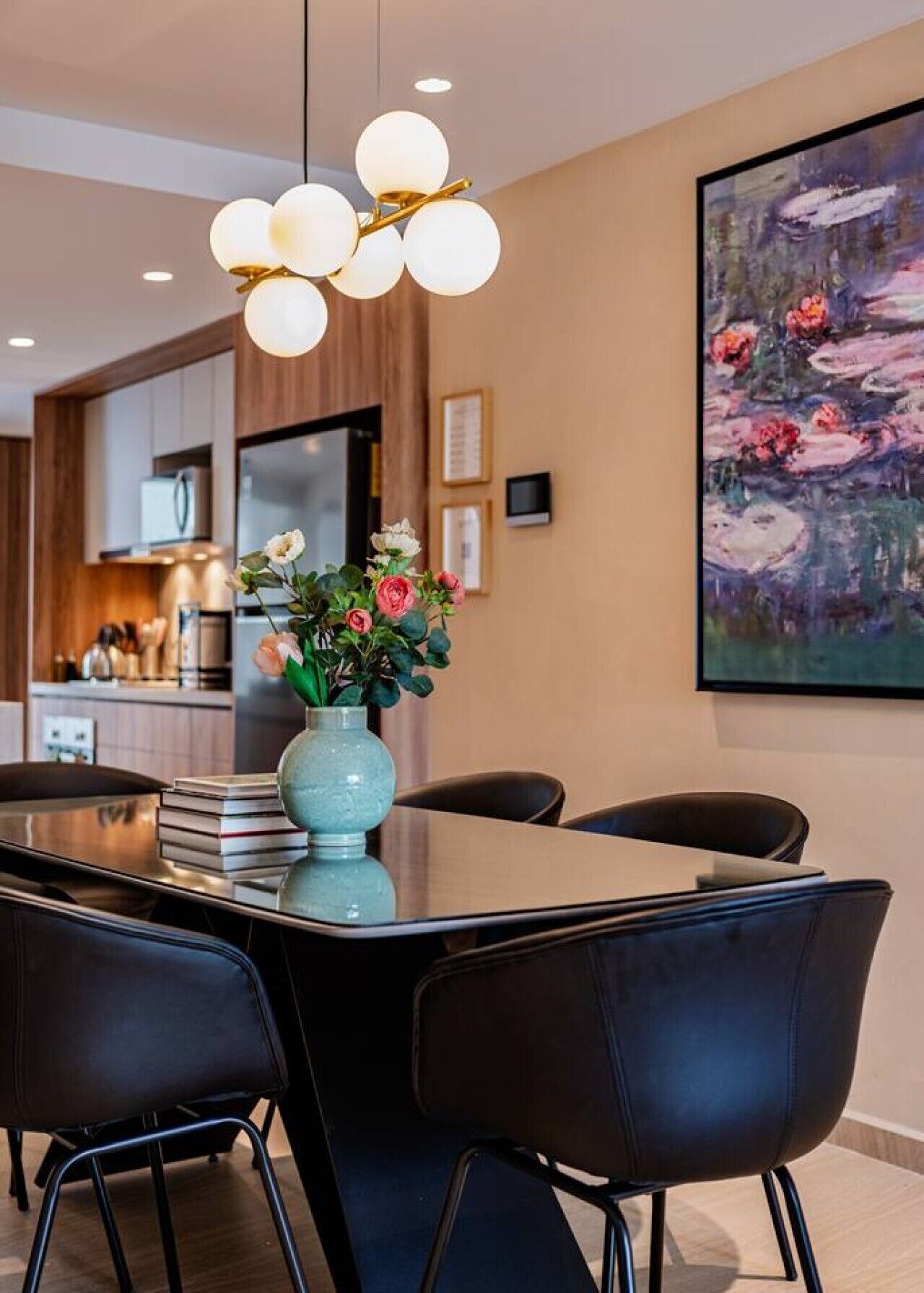 Ein Essbereich mit Tisch, Stühlen, einer Vase mit Blumen, einem Gemälde an der Wand und einer Küche im Hintergrund.