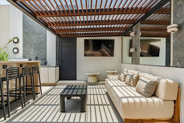 A modern outdoor living space with a wooden pergola, a sofa, a dining area with chairs, a small table, and a kitchen area with a sink and cabinets. - Condesa Apartment Near Parque México & Roma (Mexico City)