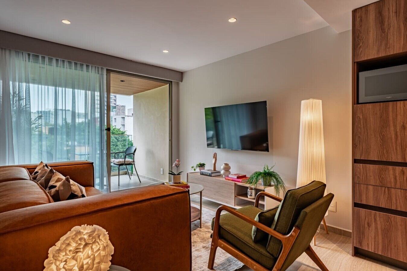 A modern living room with a sofa, a chair, a TV, and a large window.