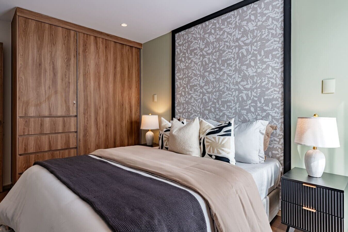 Una habitación de hotel con cama, lámparas de noche, armario y cabecero estampado.