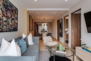 A modern living room with a grey sofa, a coffee table, and a TV. There is a dining area in the background with a table and chairs. - Spacious Condesa Apartment Near Cafés & Parks (Mexico City)