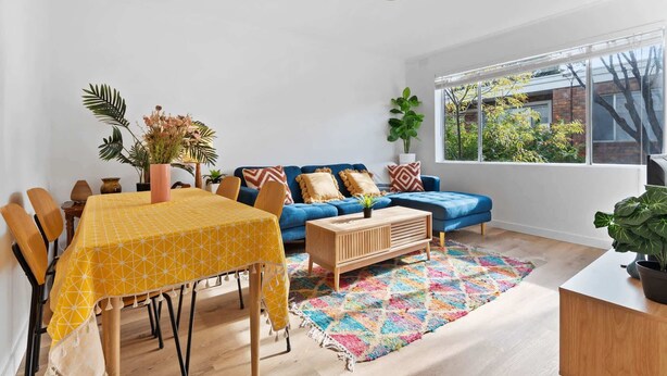 Ett modernt vardagsrum med ett matbord, en blå soffa och ett stort fönster.