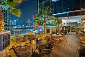 Un bar en la azotea con muebles de mimbre, vista al horizonte de la ciudad y un letrero que dice 'PAR REGIS'.