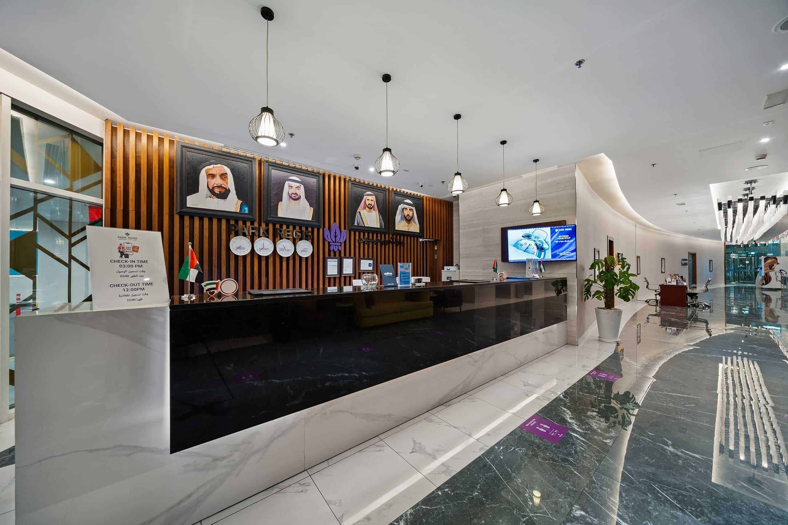 A hotel reception area with a marble counter, framed portraits, and a television screen.