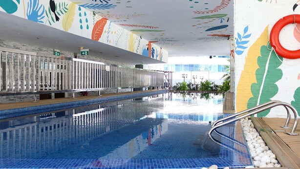 A swimming pool with a tiled floor, metal handrails, and a colorful mural on the walls.