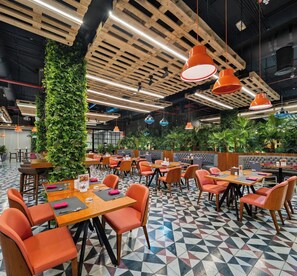 Un restaurant avec des poutres en bois au plafond, des luminaires suspendus de couleur orange et un sol orné de motifs géométriques.