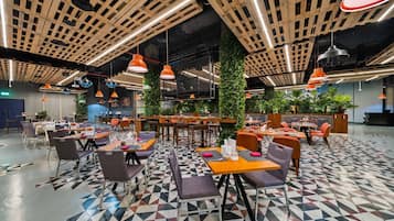 Een modern restaurant met een vloer met geometrisch patroon, houten balken in het plafond en oranje hanglampen.