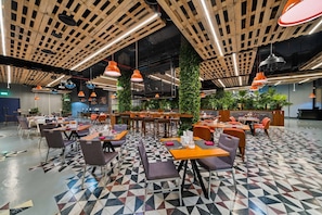 Un restaurant moderne avec un sol à motifs géométriques, des poutres en bois au plafond et des luminaires suspendus de couleur orange.