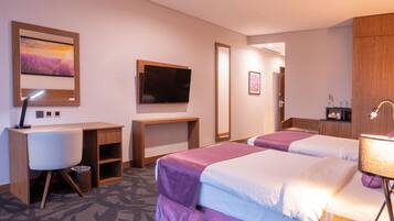 Een hotelkamer met twee bedden, een bureau, een televisie en een kast.