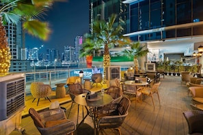 A rooftop bar with wicker furniture, a view of the city skyline, and a sign for 'PAR REGIS.'