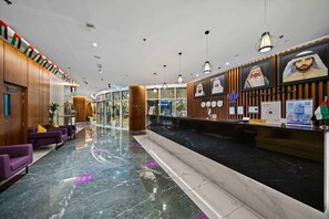 Vestíbulo de hotel con mostrador de recepción, asientos morados y piso de mármol.