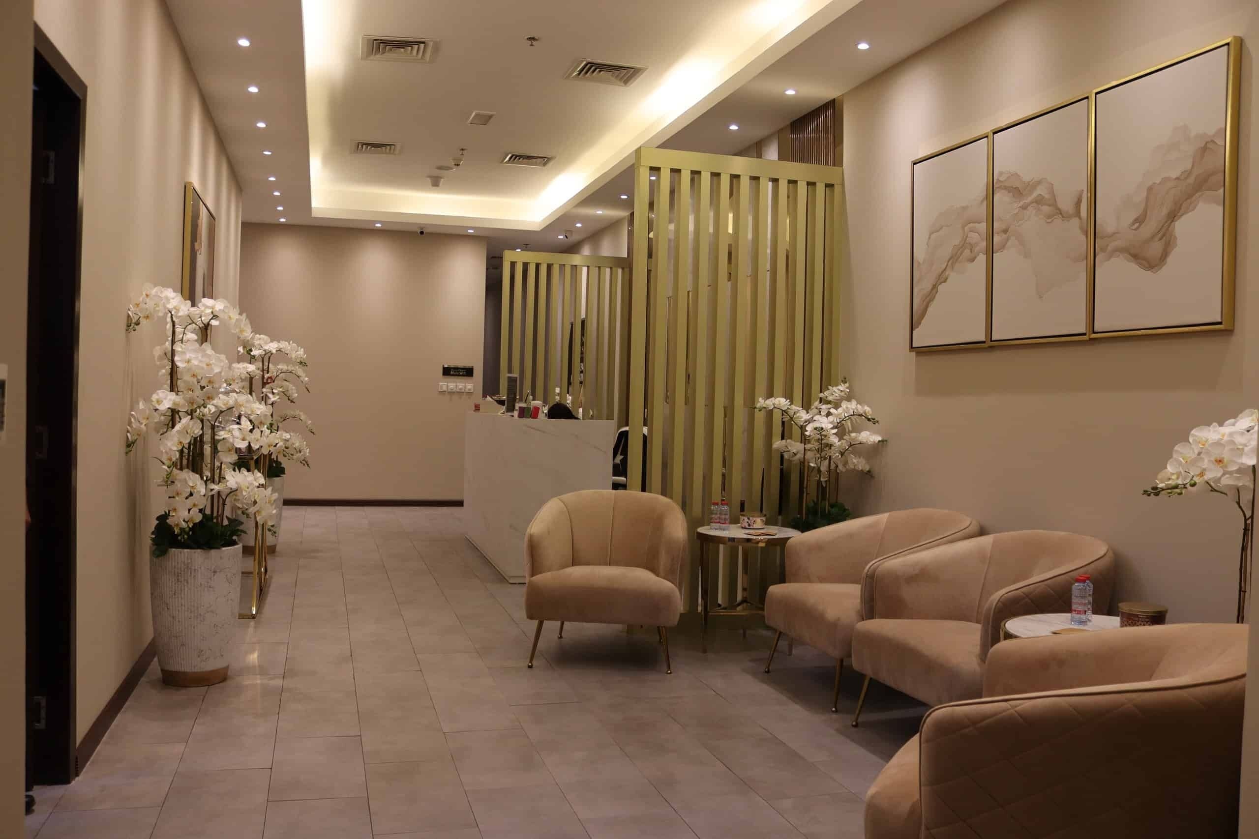 Un hall d’hôtel comprenant un comptoir d’accueil, un espace salon et des éléments décoratifs tels que des orchidées et des œuvres d’art.
