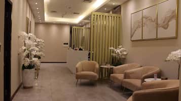 Un hall d’hôtel comprenant un comptoir d’accueil, un espace salon et des éléments décoratifs tels que des orchidées et des œuvres d’art.