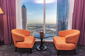 Habitación de hotel con dos sillones de estampado naranja, una mesita redonda y un ventanal con vistas a la ciudad.