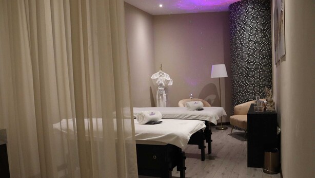 A hotel room with two beds, a sitting area, a lamp, and a decorative wall.