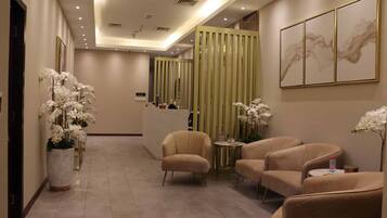 Un hall d’hôtel comprenant un comptoir d’accueil, un espace salon et des éléments décoratifs tels que des orchidées et des œuvres d’art.