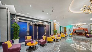 Un lobby moderno con zonas de estar, un mostrador de recepción y un cartel que dice 'GOOD DAY'.
