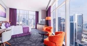 Une chambre d’hôtel avec un lit, un bureau, deux chaises, une télévision et une vue sur le paysage urbain.