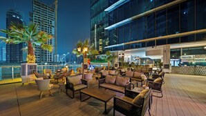 Un bar en la azotea con mesas al aire libre, palmeras y el horizonte de la ciudad de fondo.